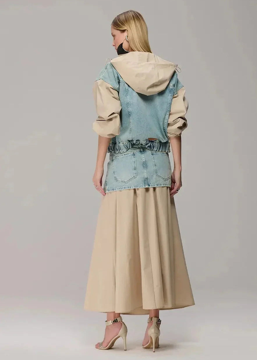 Woman wearing a layered outfit with a denim jacket and beige skirt on a plain background