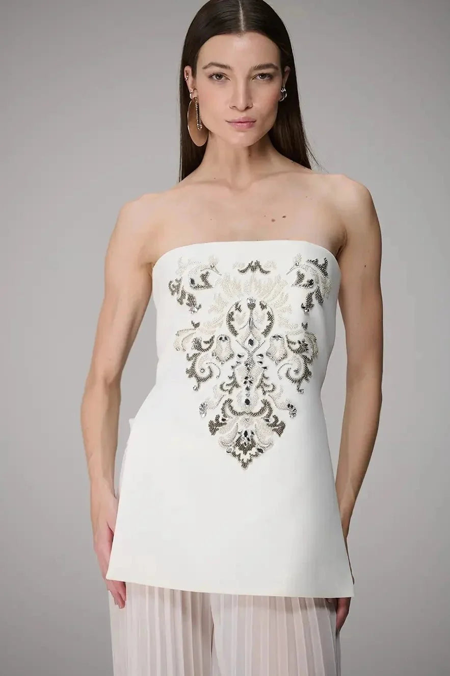 Woman wearing a white strapless dress with intricate black embroidery on a gray background