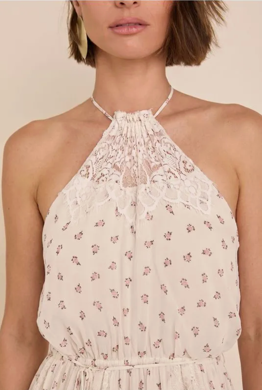 Close-up of a model wearing a cream-colored halter dress with a delicate pink floral print and a lace halter neckline.
