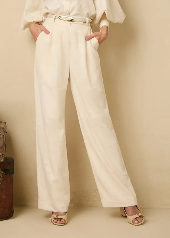 Woman in a white outfit standing next to vintage suitcases against a beige wall.