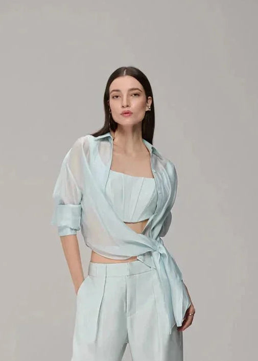 A model stands in a studio wearing a light mint green two-piece outfit consisting of a cropped wrap-style top and matching wide-leg pants with sheer overlay panels.