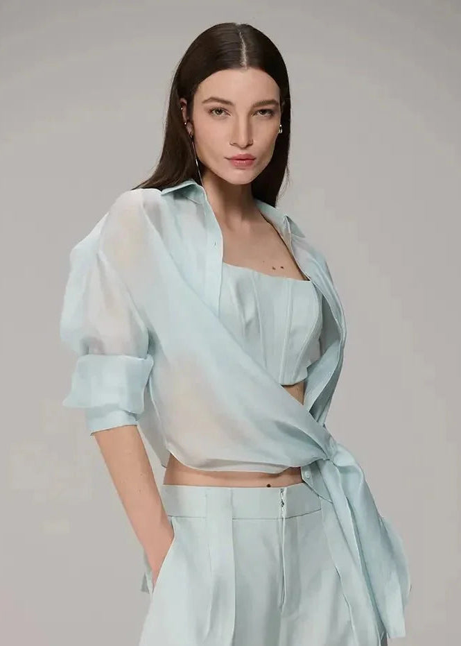 Woman wearing a light blue outfit with a sheer top and wide-leg pants on a gray background