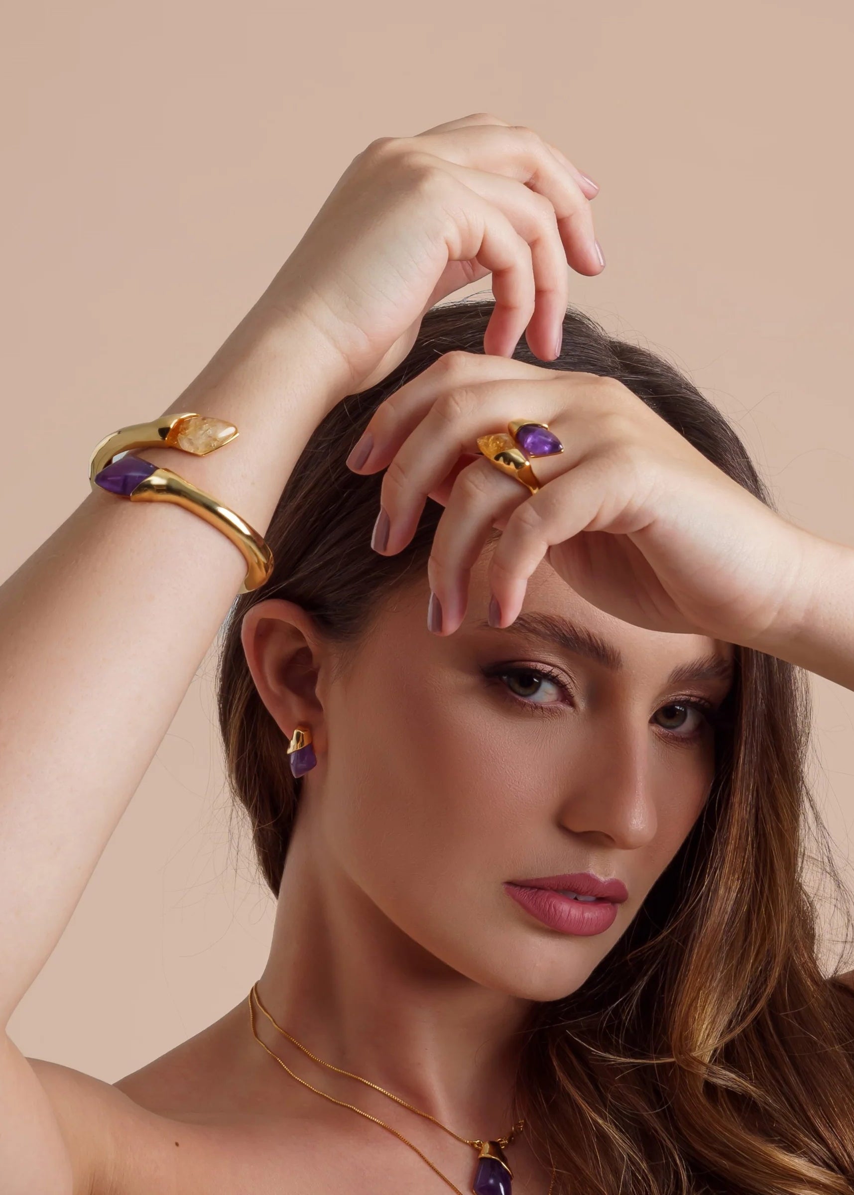 Woman wearing gold jewelry with purple gemstones on a beige background