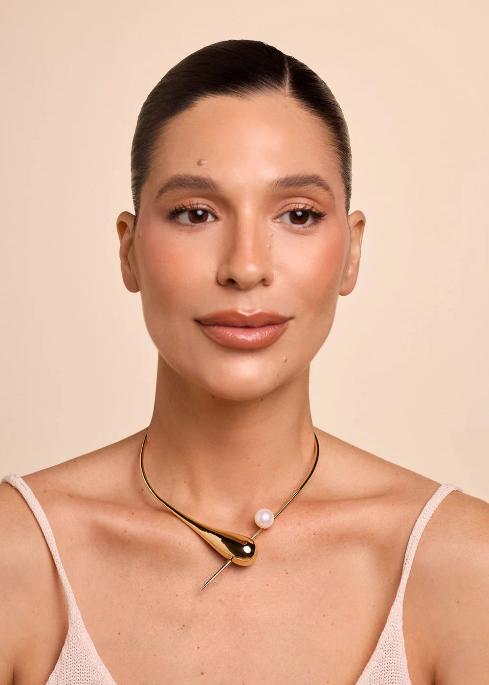 Woman wearing a gold necklace with a pearl pendant against a beige background