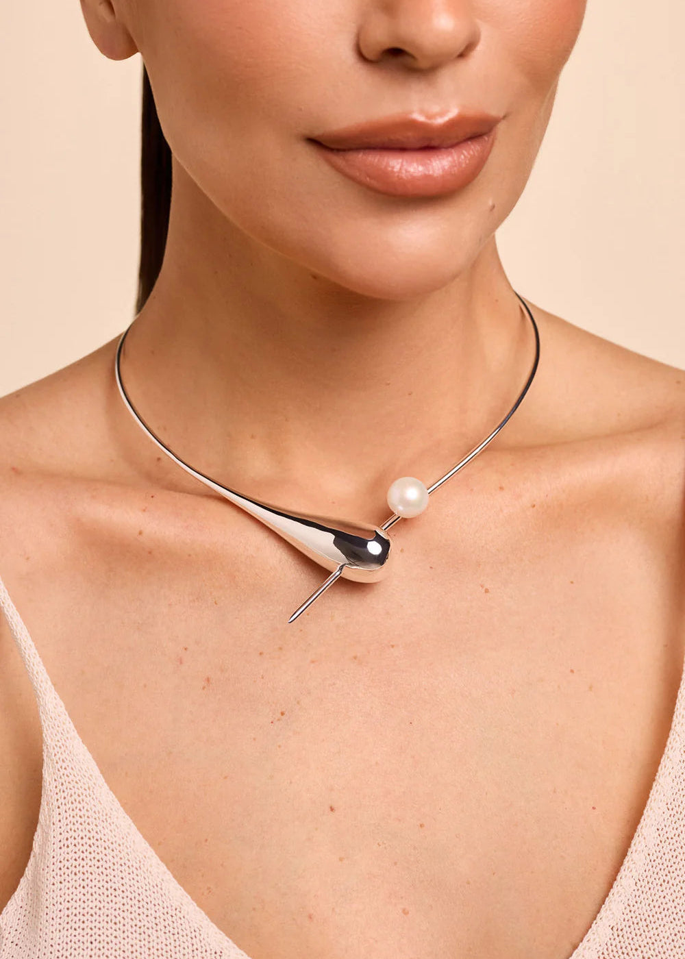 Necklace with a pearl pendant worn by a person on a beige background