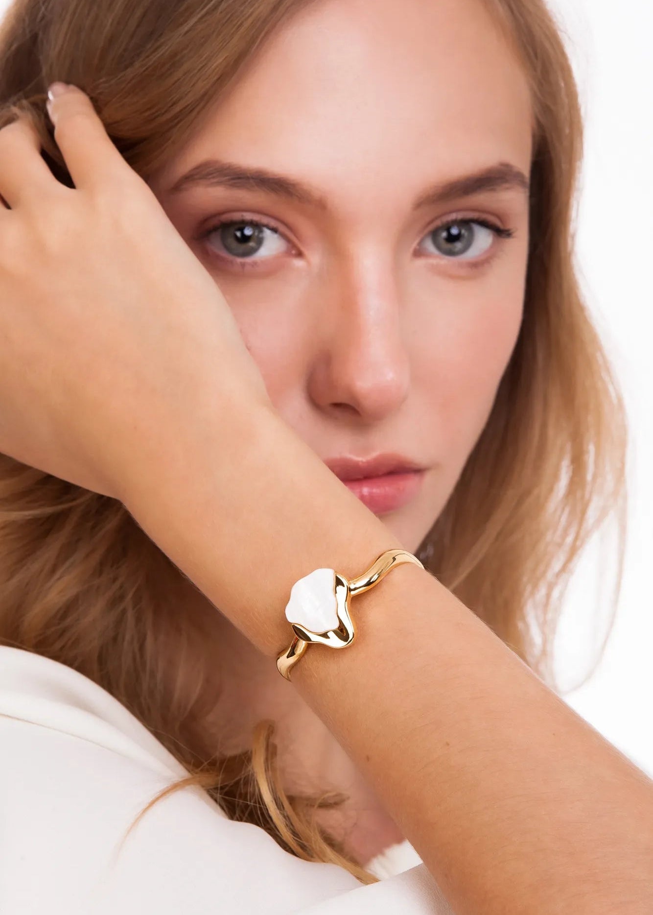 Woman wearing a gold bracelet with a heart-shaped charm on a white background