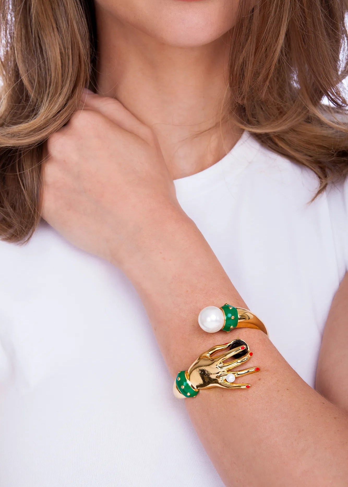 Gold bracelet with pearl and green gemstones on a person wearing a white top.