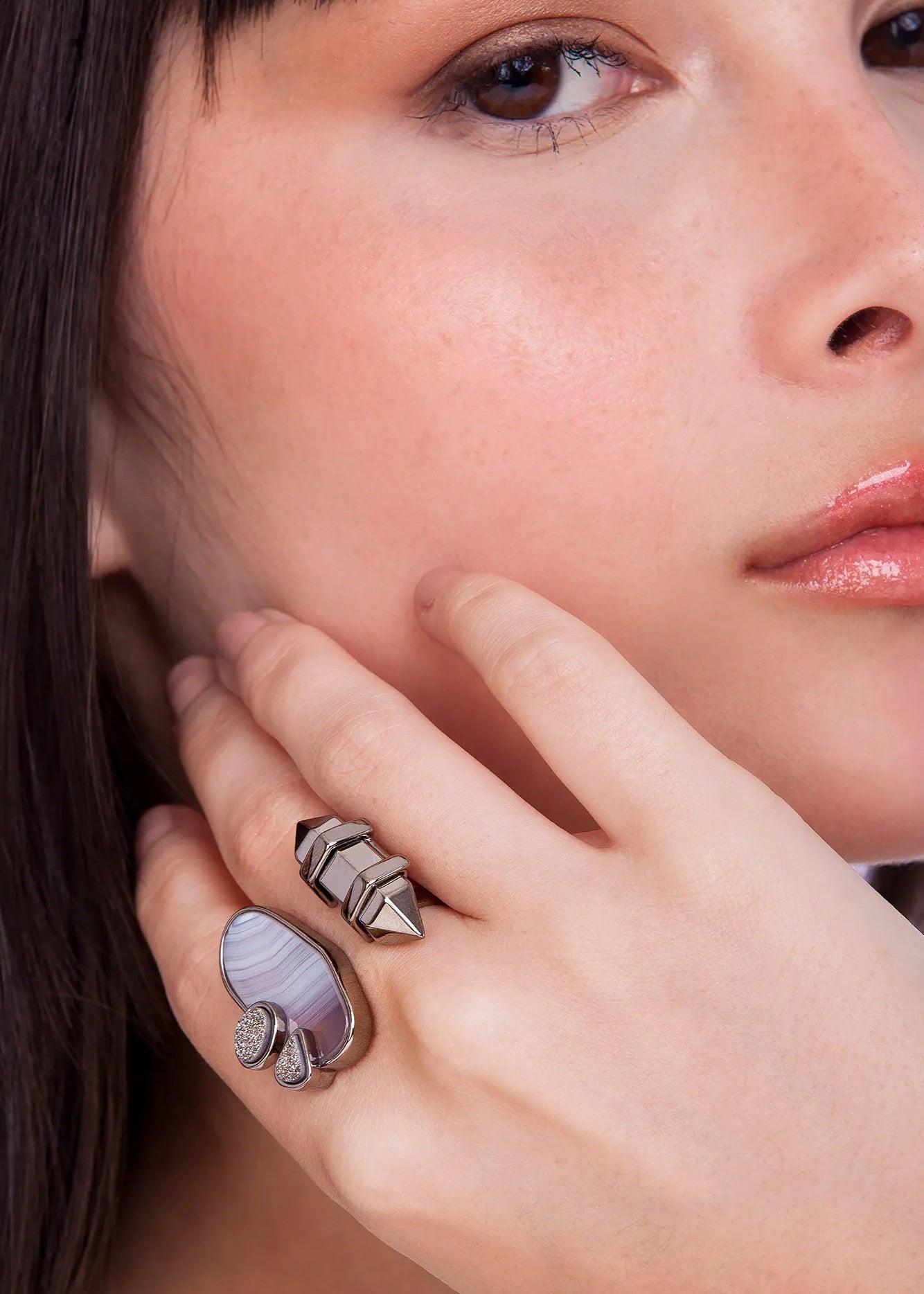 Close-up of a woman's hand wearing a ring with a purple stone, touching her face.