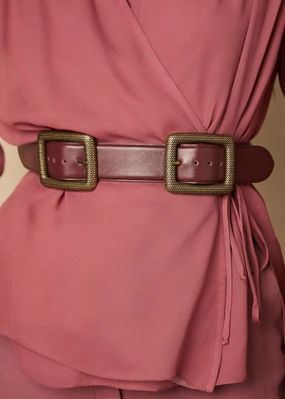 Close-up of a pink garment with a guava belt and gold buckle on a beige background
