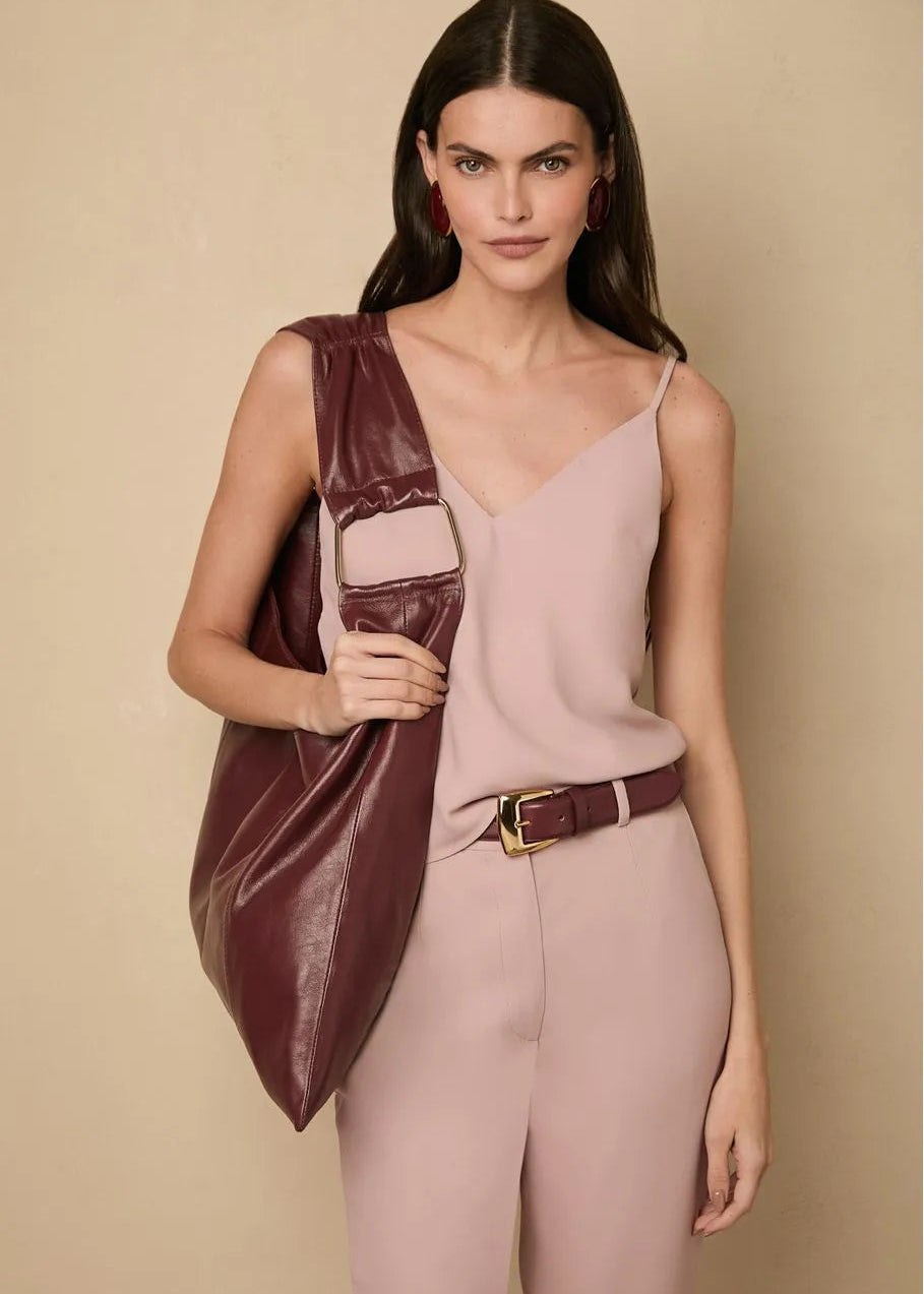 Woman wearing a pink jumpsuit with a guava colored leather bag against a beige background