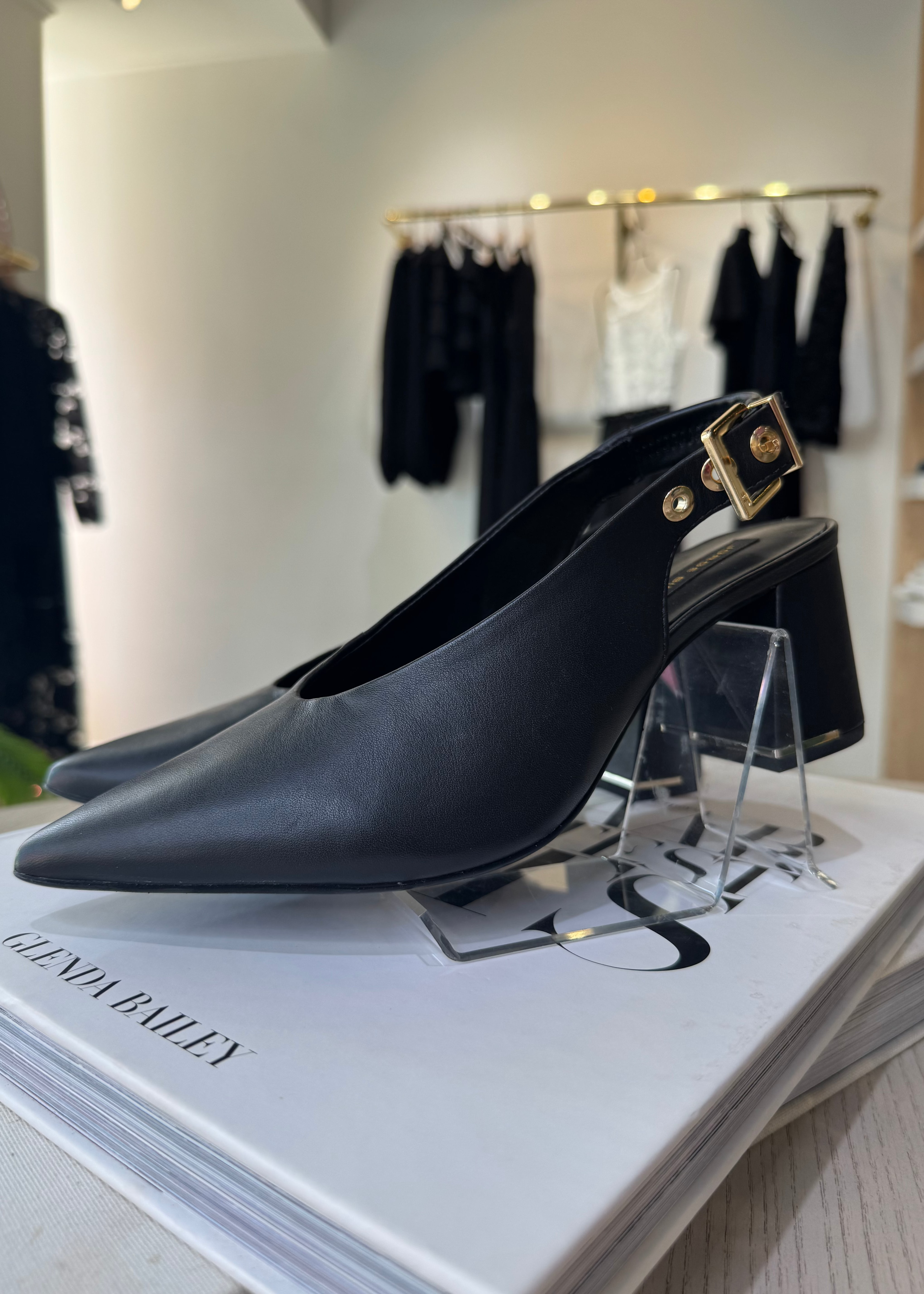 Black high-heeled shoes on a stand with a magazine underneath in a store setting