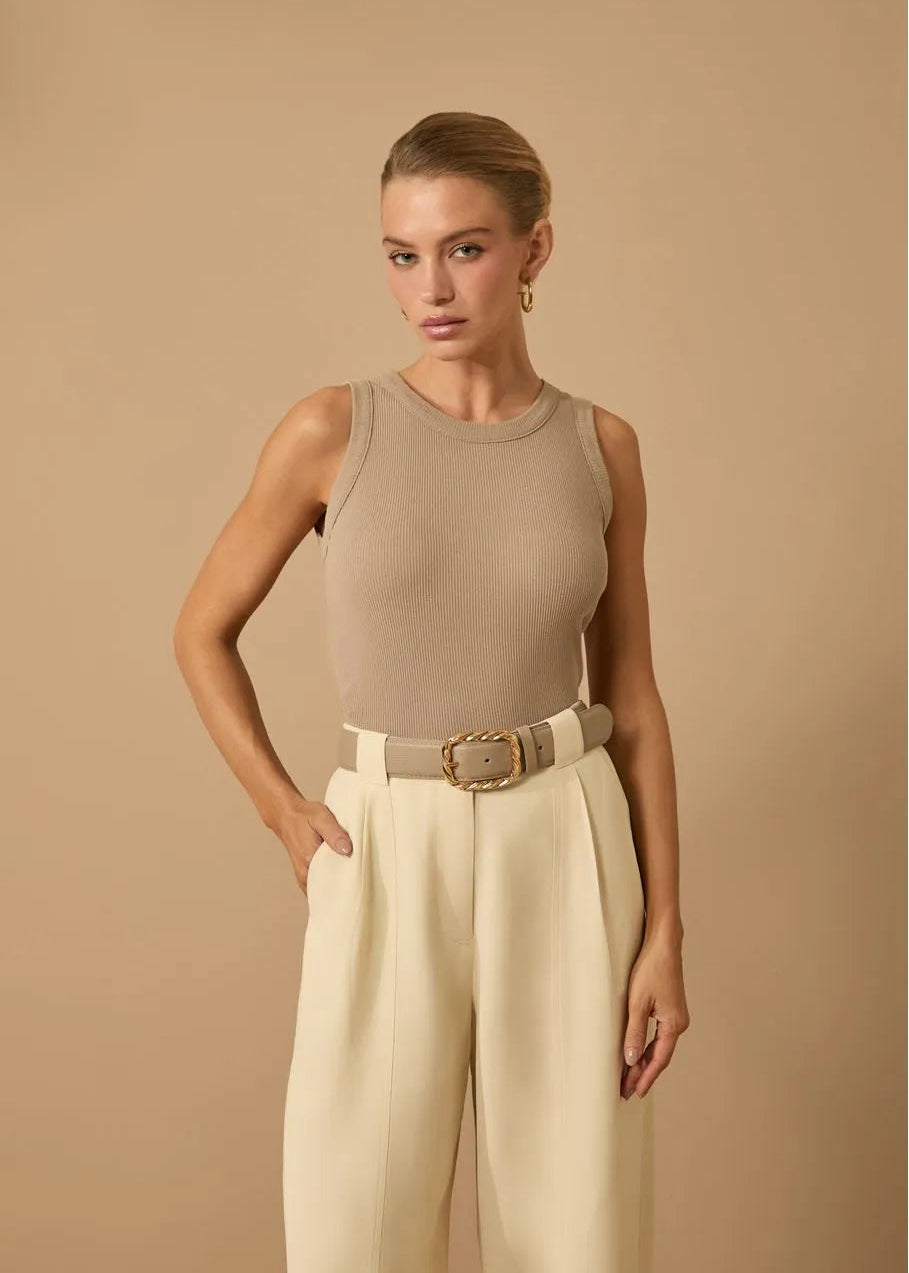 Woman wearing a beige sleeveless top and wide-leg pants against a beige background