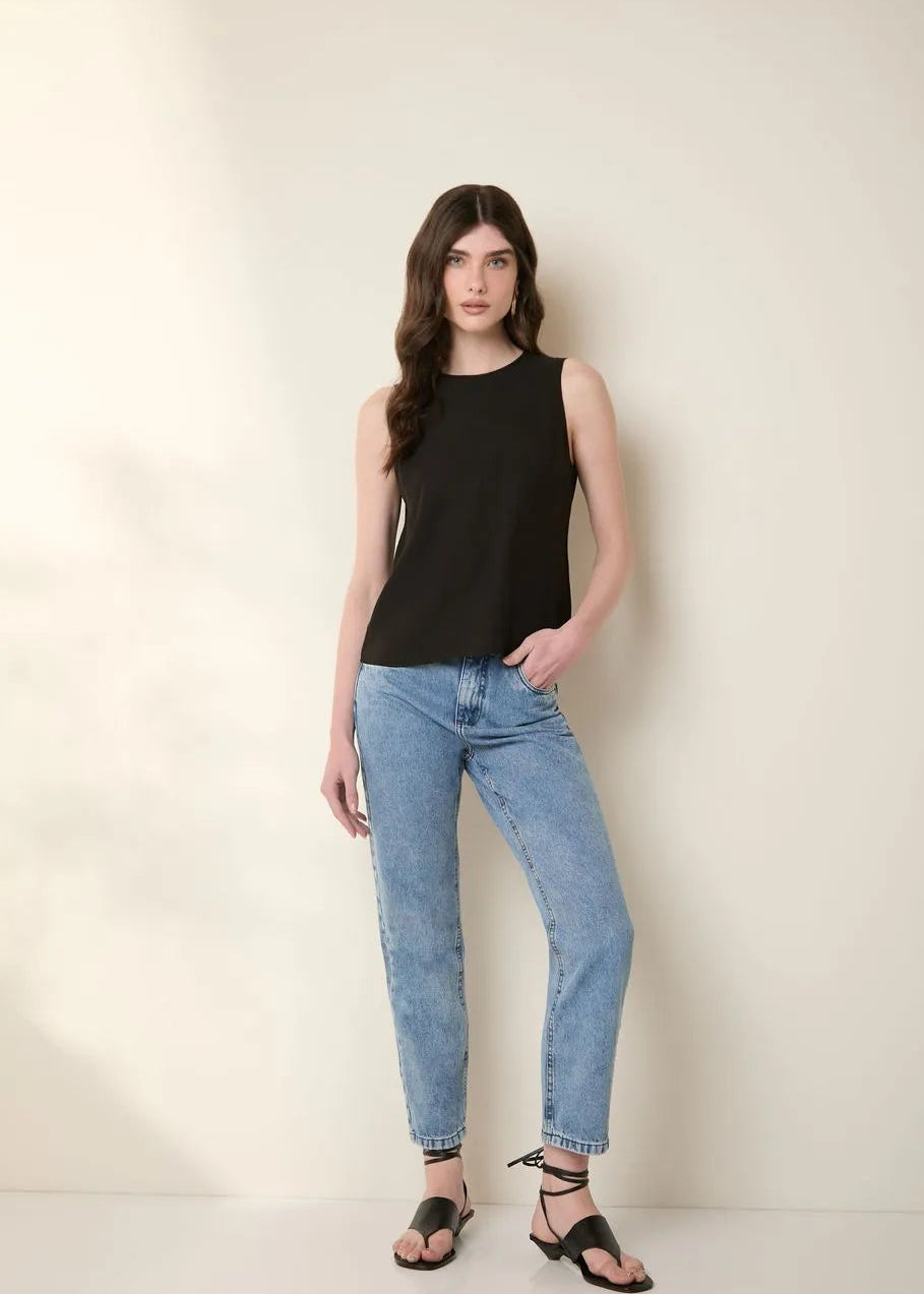 Woman wearing a black sleeveless top and blue jeans against a plain background