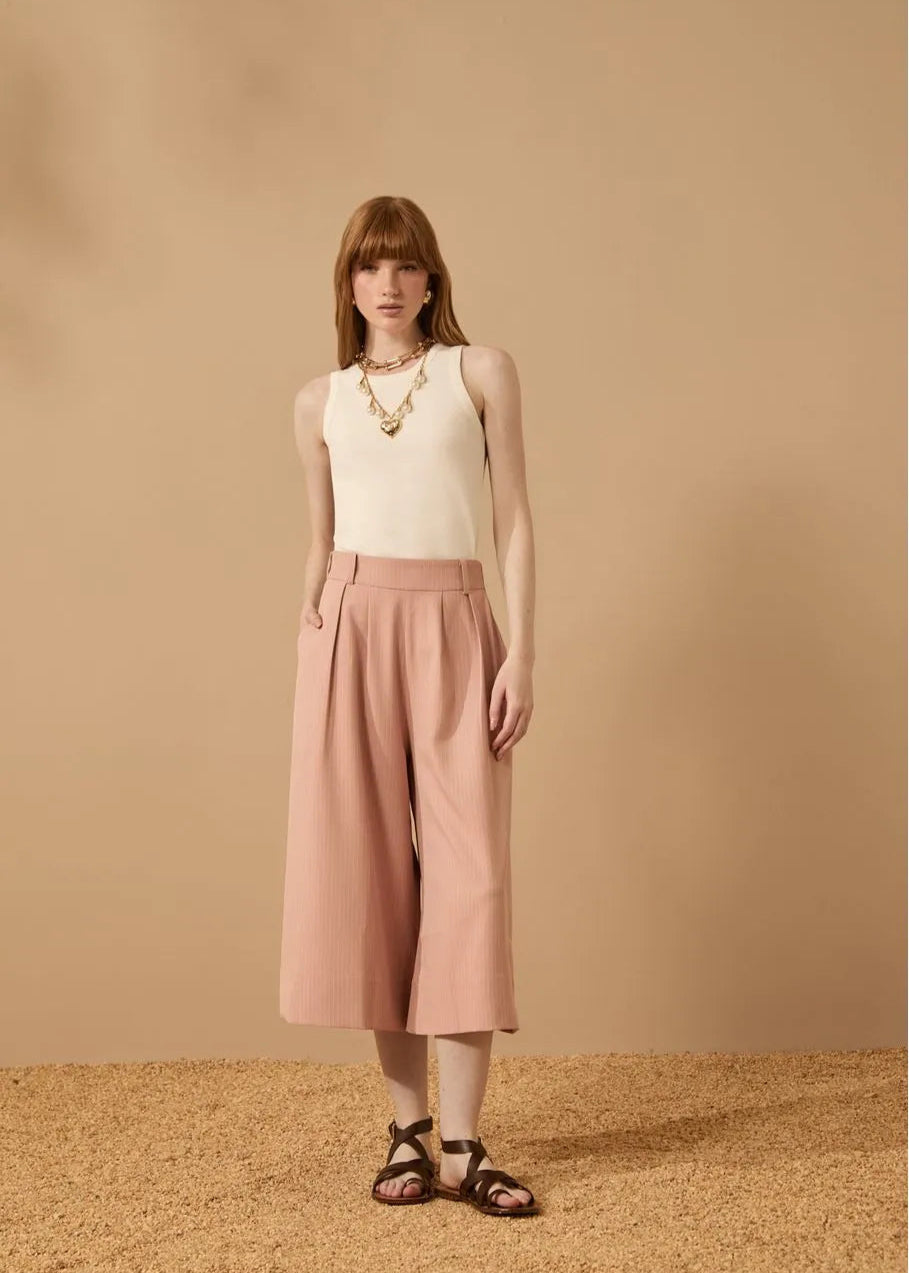 Woman wearing a white sleeveless top and pink wide-leg pants against a beige background