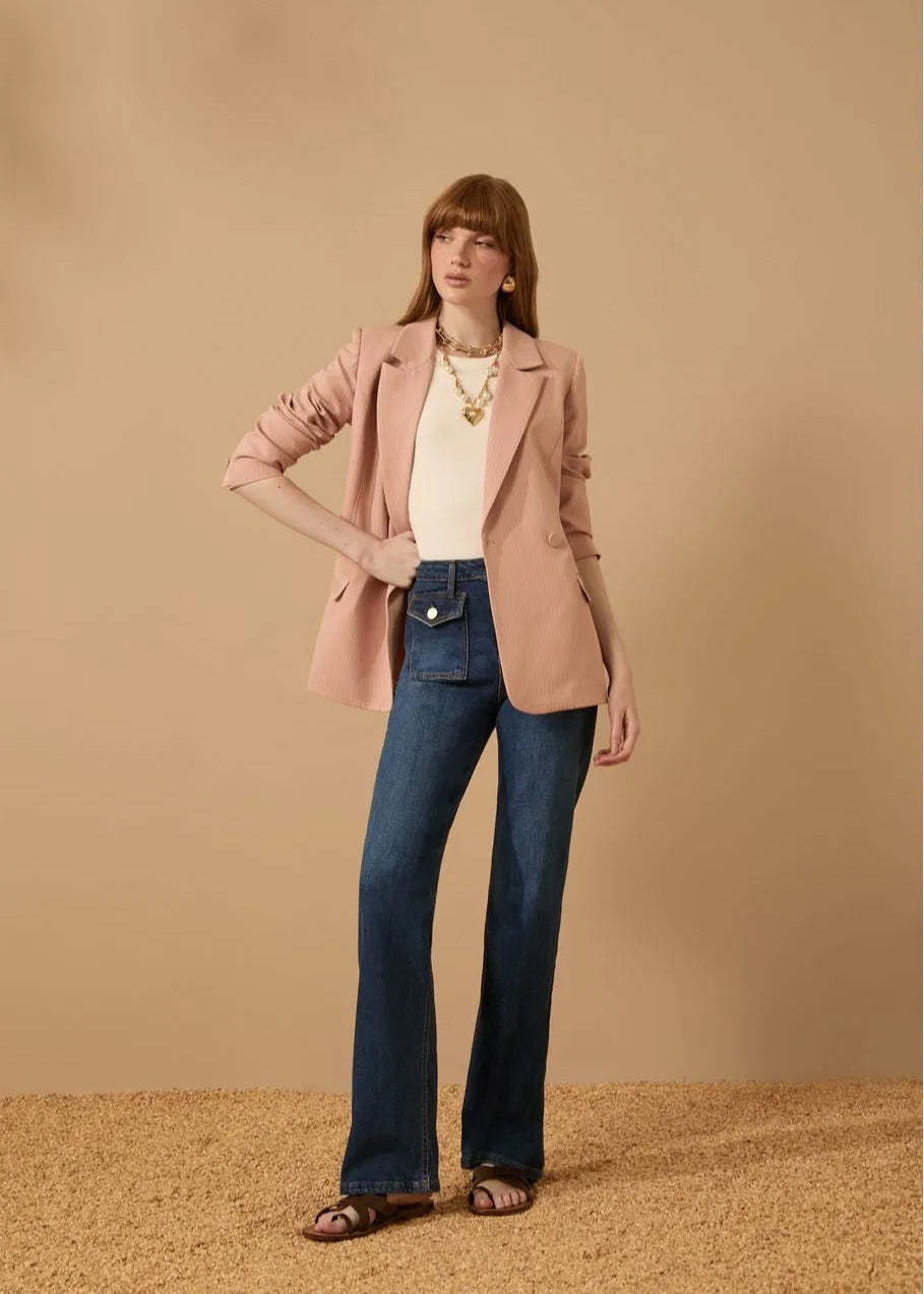 Woman wearing a pink blazer, white top, and blue jeans against a beige background