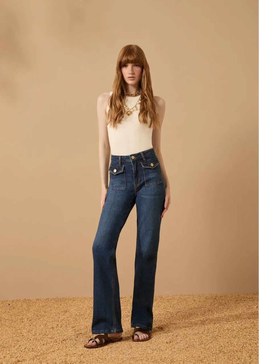 Woman wearing blue jeans and a white top against a beige background