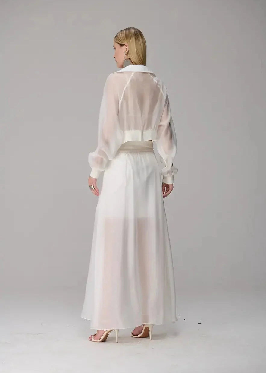 Woman wearing a sheer white blouse and long skirt on a plain background