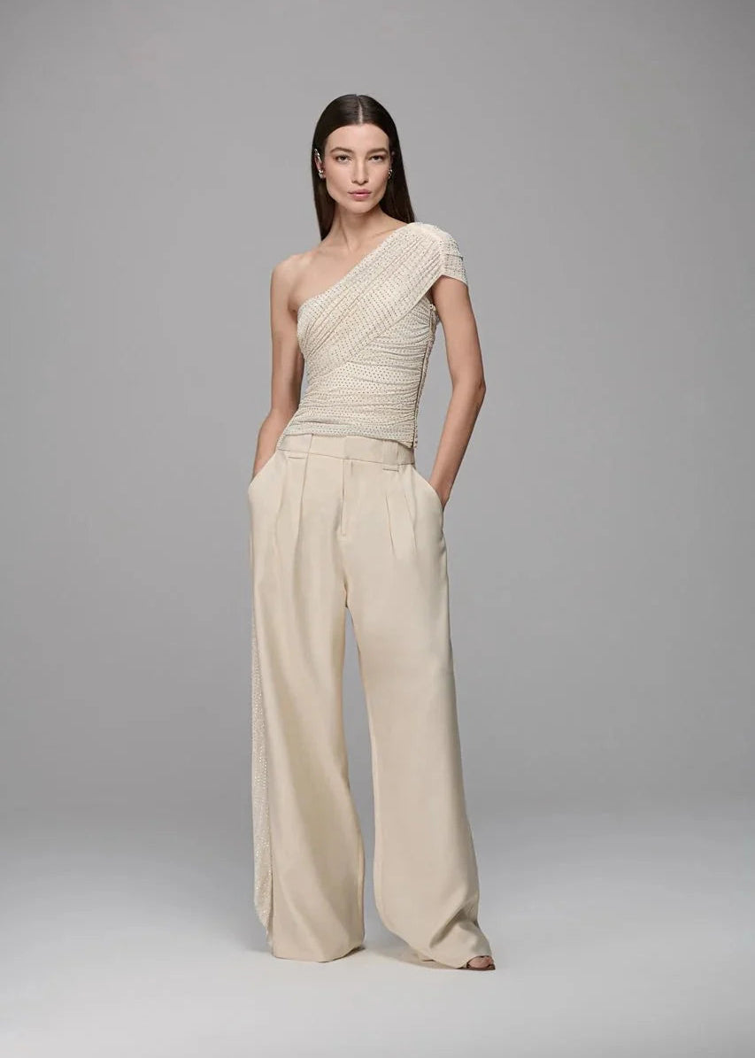 Woman wearing a beige one-shoulder jumpsuit on a gray background