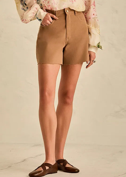 Woman wearing a floral blouse and beige shorts against a neutral background