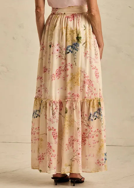 Woman wearing a pink top and floral skirt against a neutral background