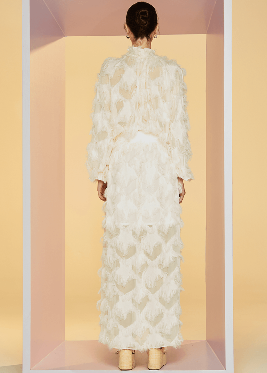 Woman wearing a white floral dress standing in a minimalistic setting with pastel pink and yellow walls.