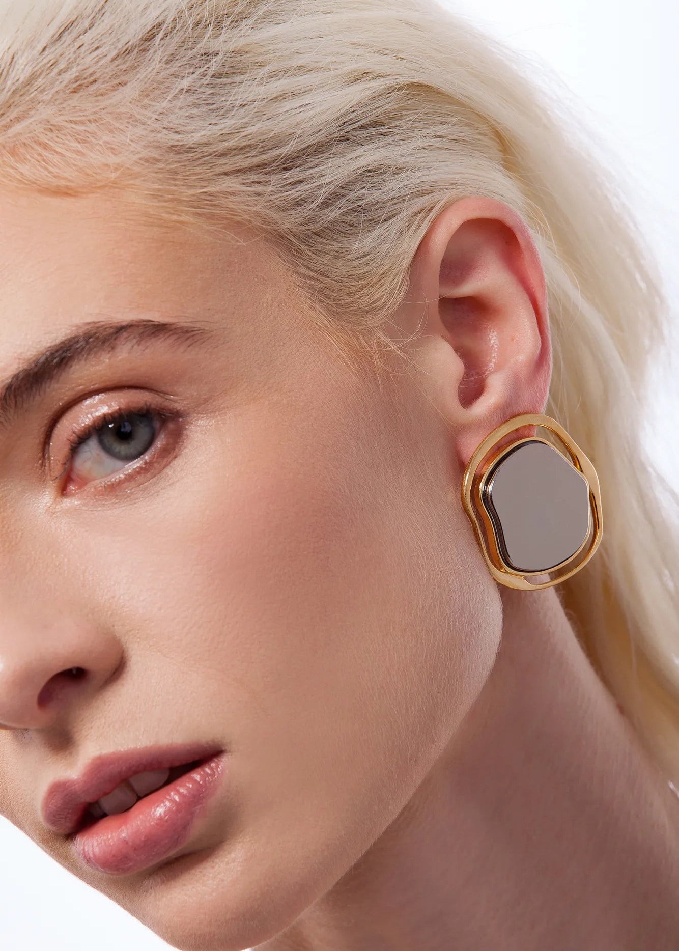 Close-up of a woman wearing a gold earring with a gray center on a white background