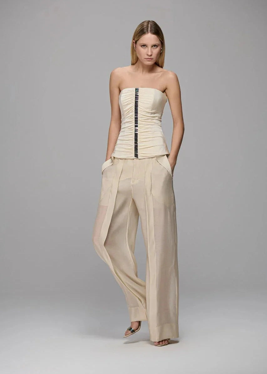 Woman wearing a strapless top and wide-leg pants on a gray background