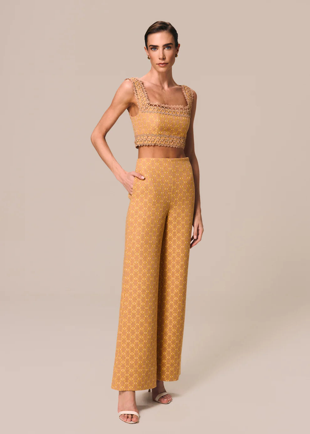 Woman wearing a mustard yellow outfit with a patterned top and wide-leg pants on a beige background