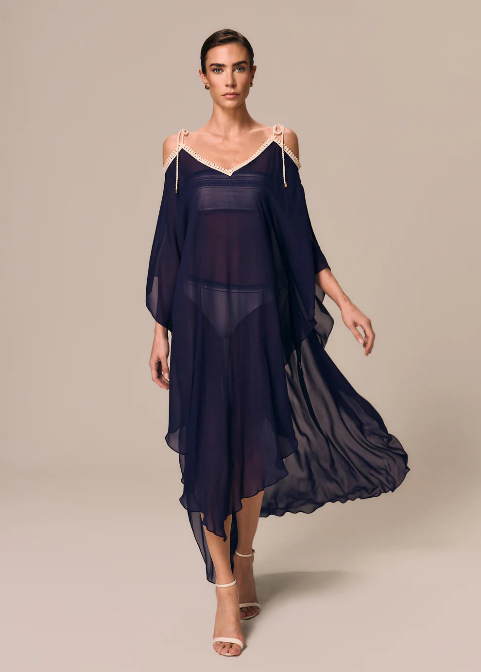 Woman wearing a dark blue dress with sheer sleeves on a beige background