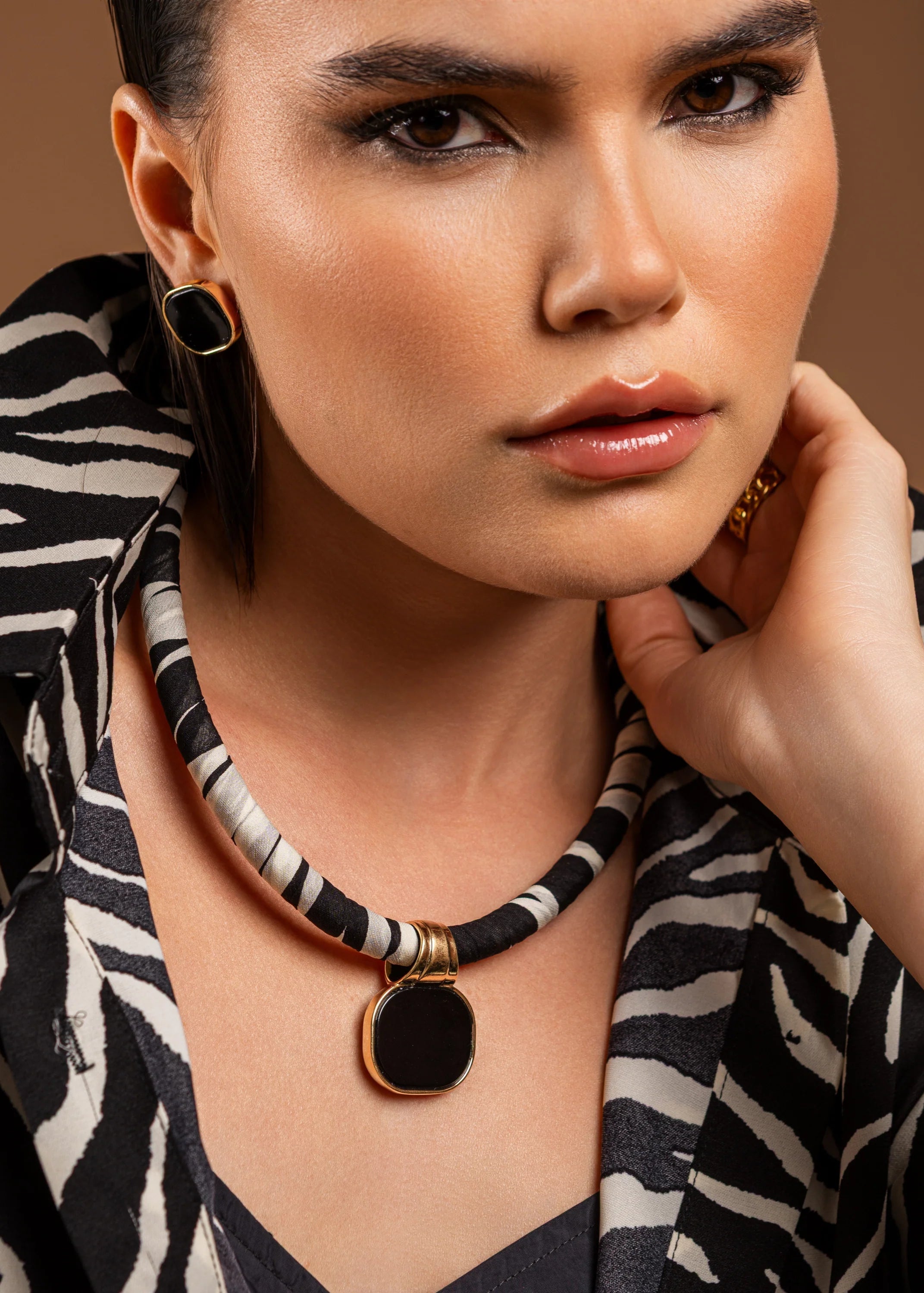 Woman wearing a black and white patterned top with a necklace and earrings against a brown background