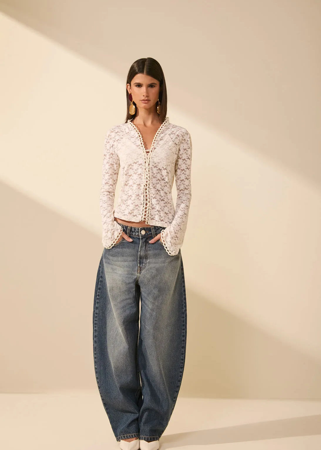 Woman wearing a white lace top and blue jeans on a beige background