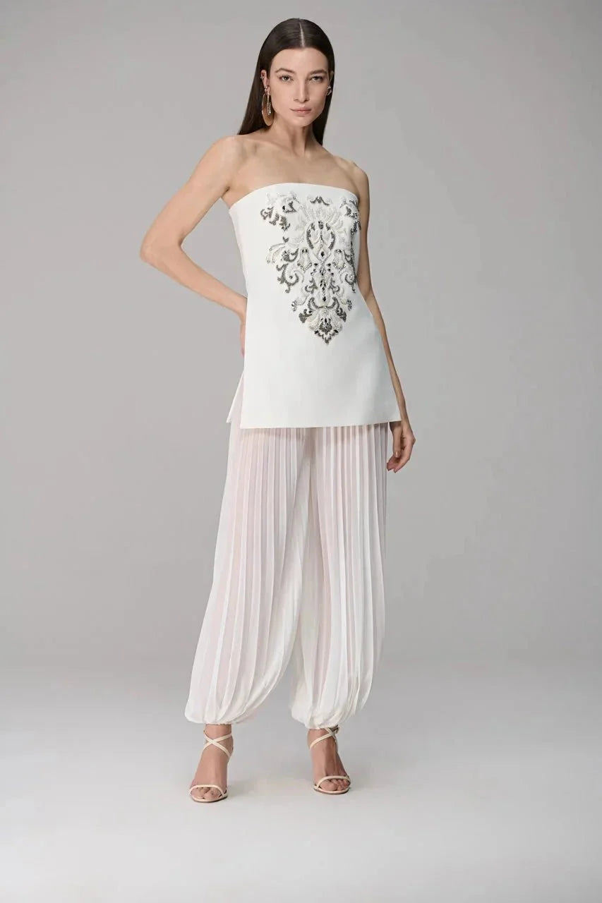 Woman wearing a strapless top with floral embroidery and sheer pants on a gray background