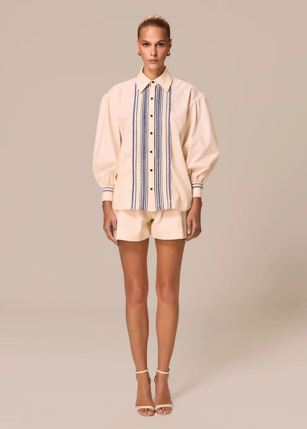 Woman wearing a beige shirt with a striped pattern and shorts on a beige background