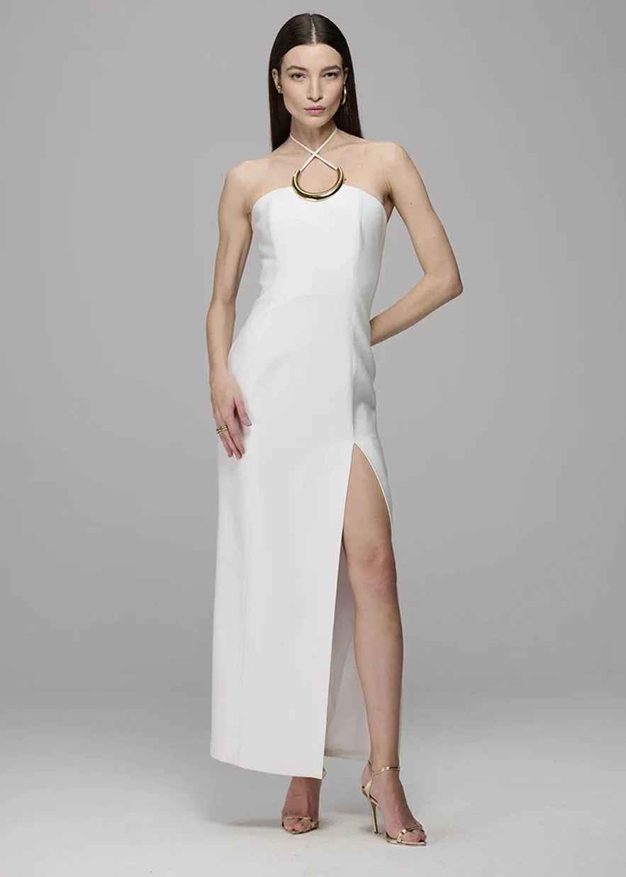 Woman wearing a white halter neck dress with a high slit on a gray background