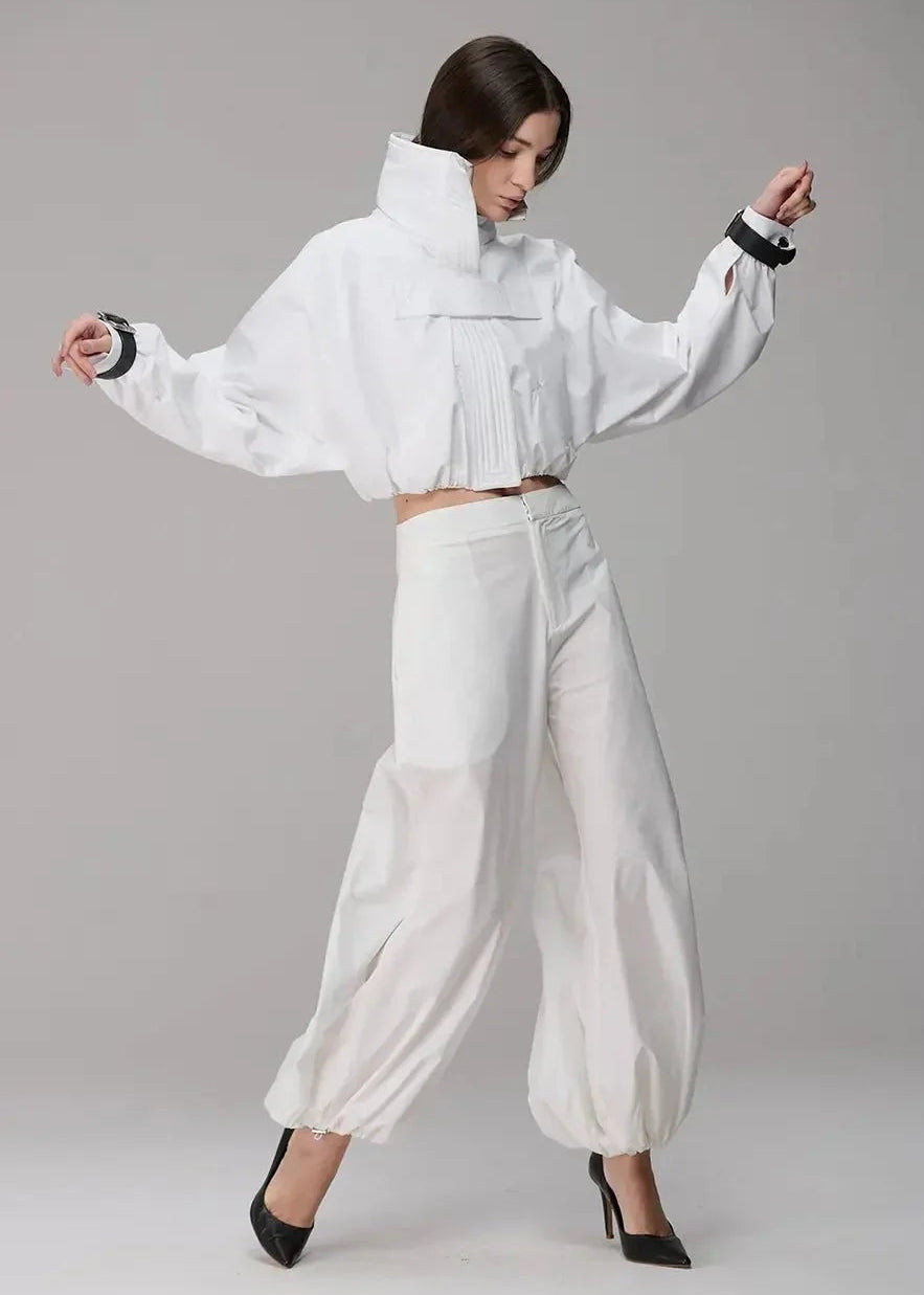 Person wearing a white outfit with wide sleeves and high-waisted pants on a gray background