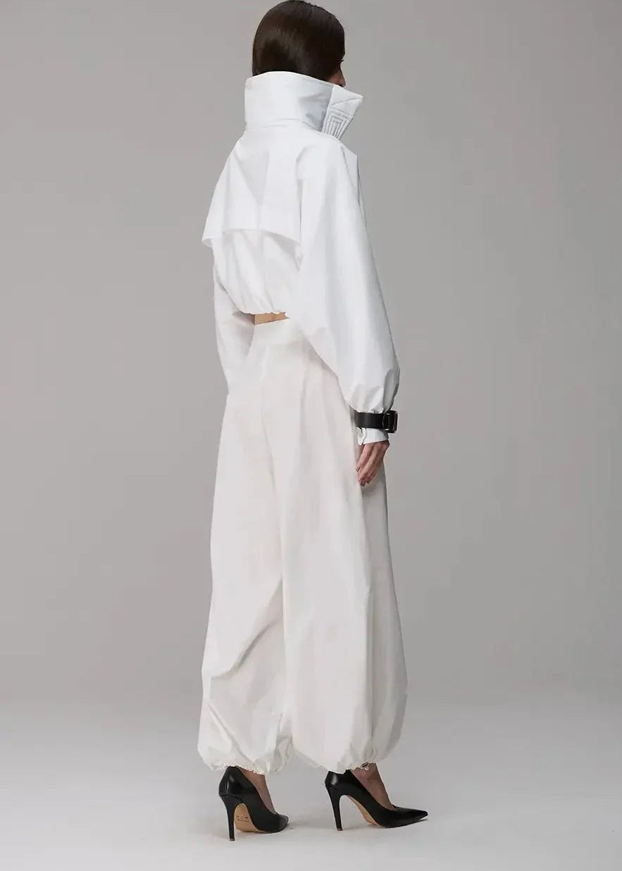 Person wearing a white outfit with a high collar on a gray background