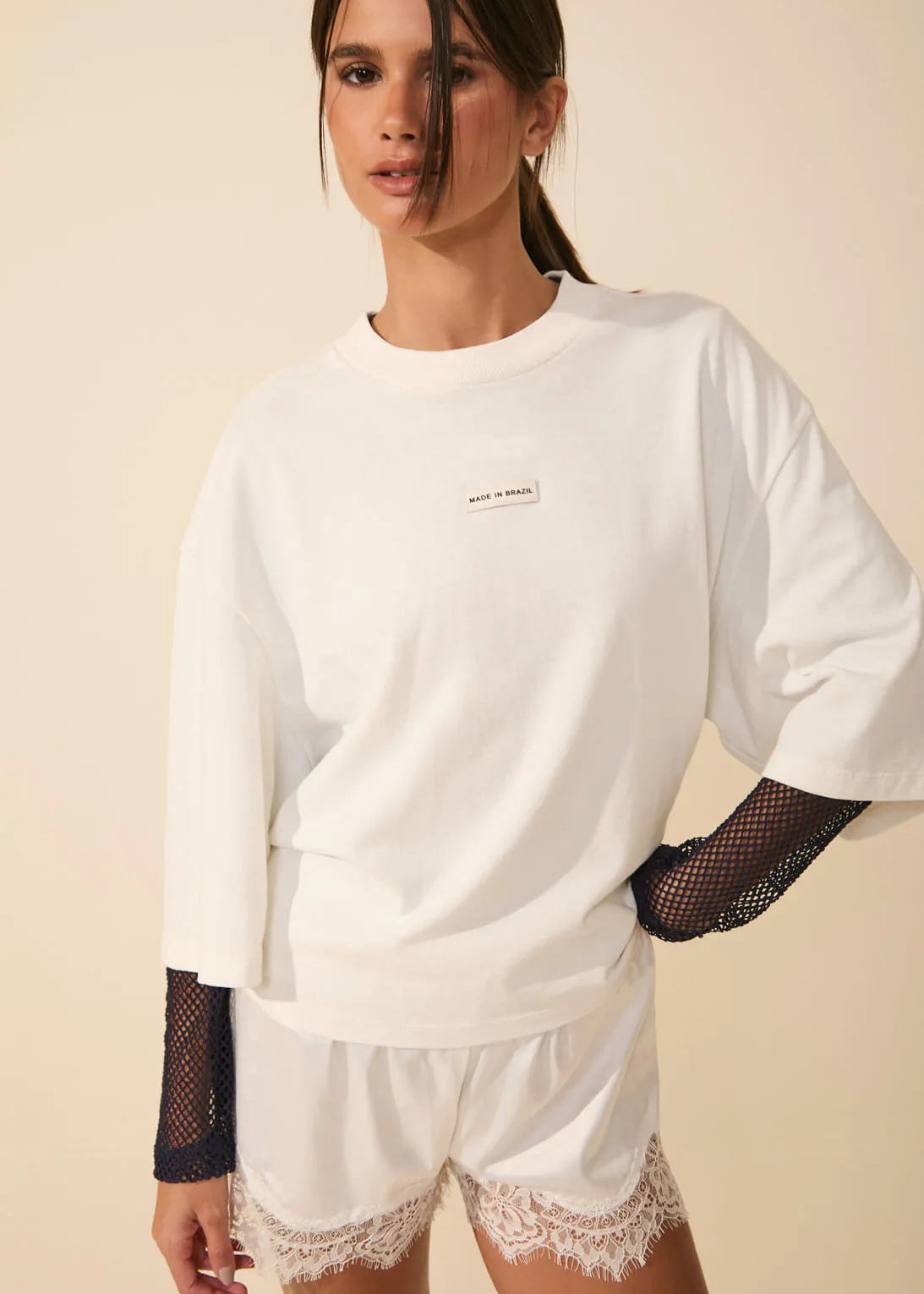 Woman wearing a white oversized sweatshirt with sheer sleeves and lace shorts on a beige background