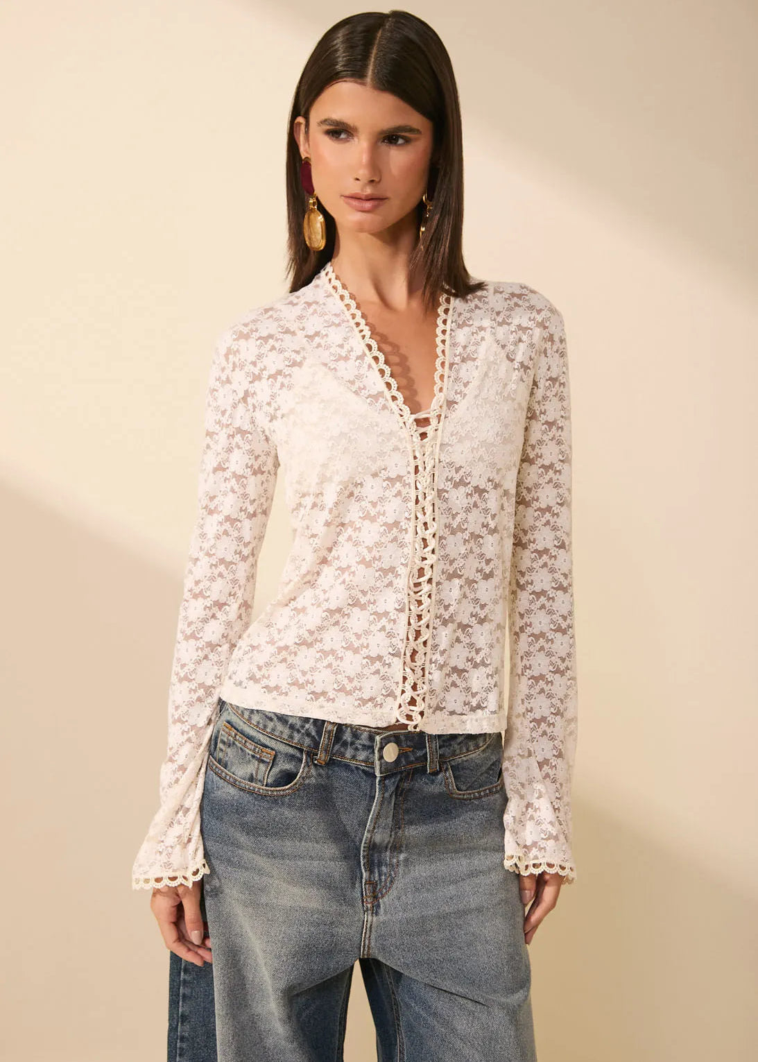 Woman wearing a lace blouse and jeans against a beige background