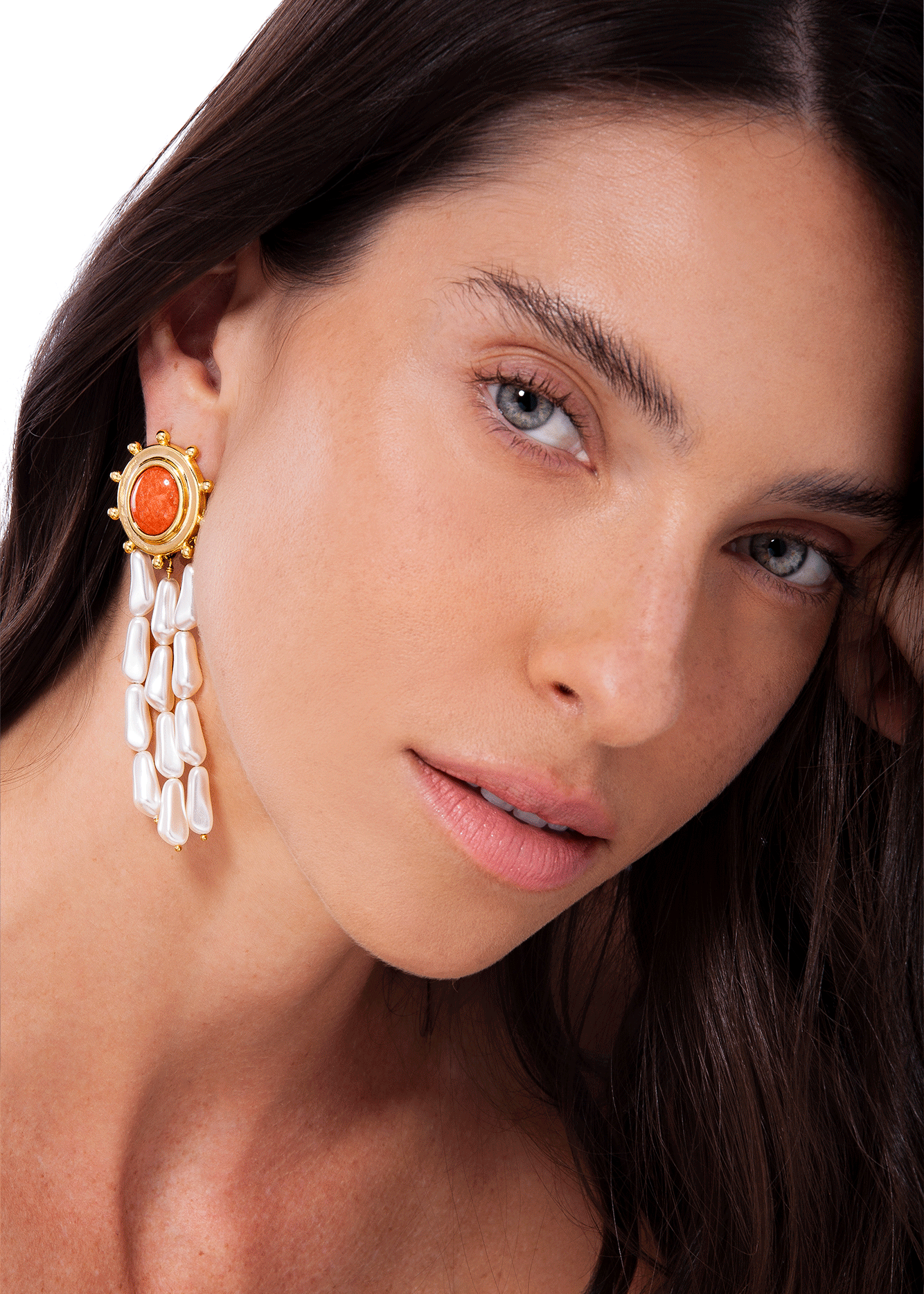 Close-up of a woman wearing a gold earring with a red stone and pearl-like drops.