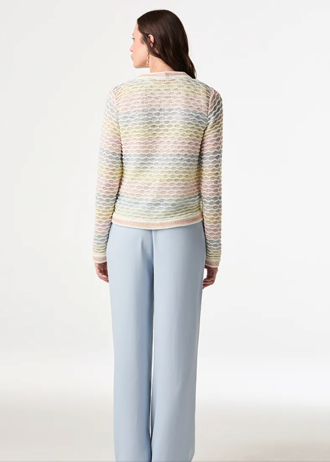 A woman is shown from the back wearing a pastel striped knit sweater and light blue wide-leg trousers against a plain white studio background.
