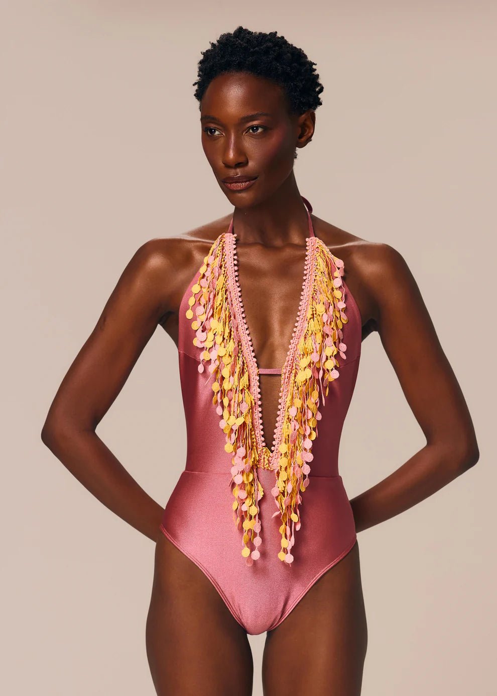 Model wearing a pink swimsuit with floral embellishments against a beige background