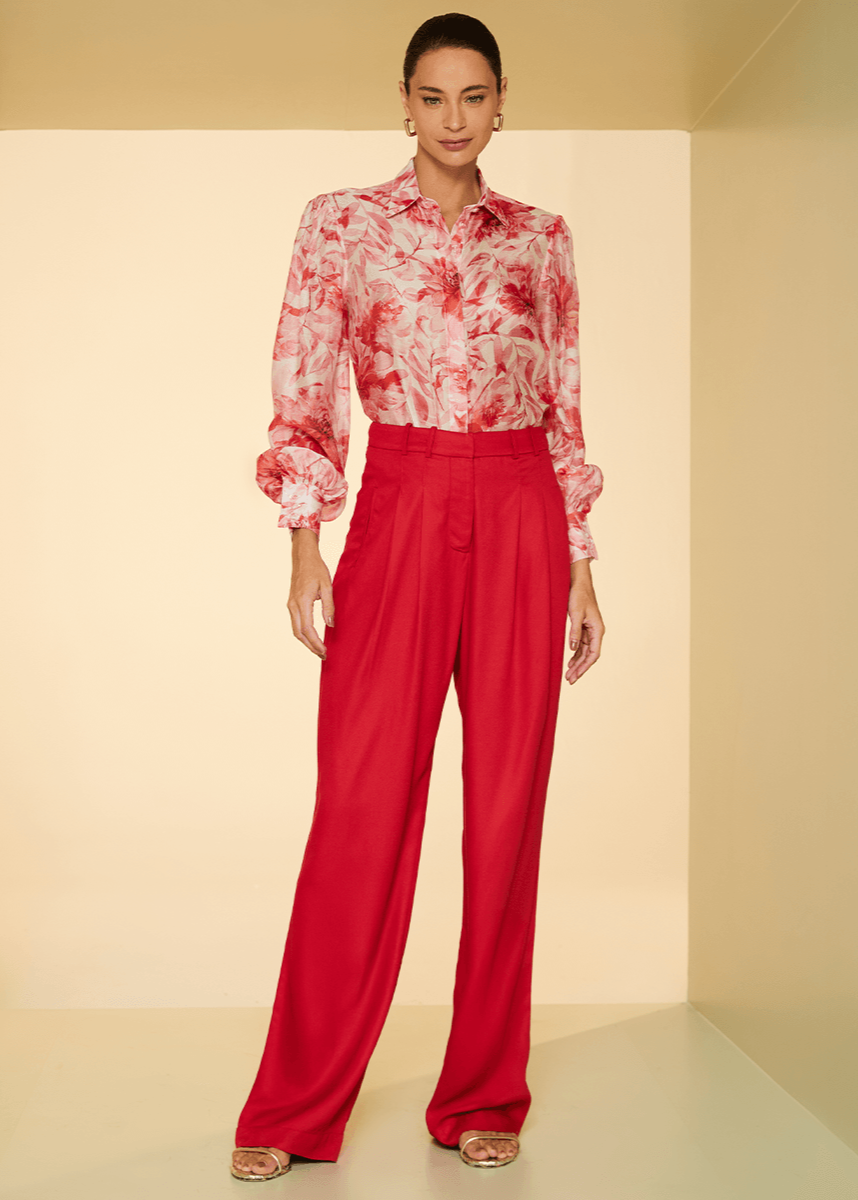 Woman wearing a red floral blouse and red pants against a beige background
