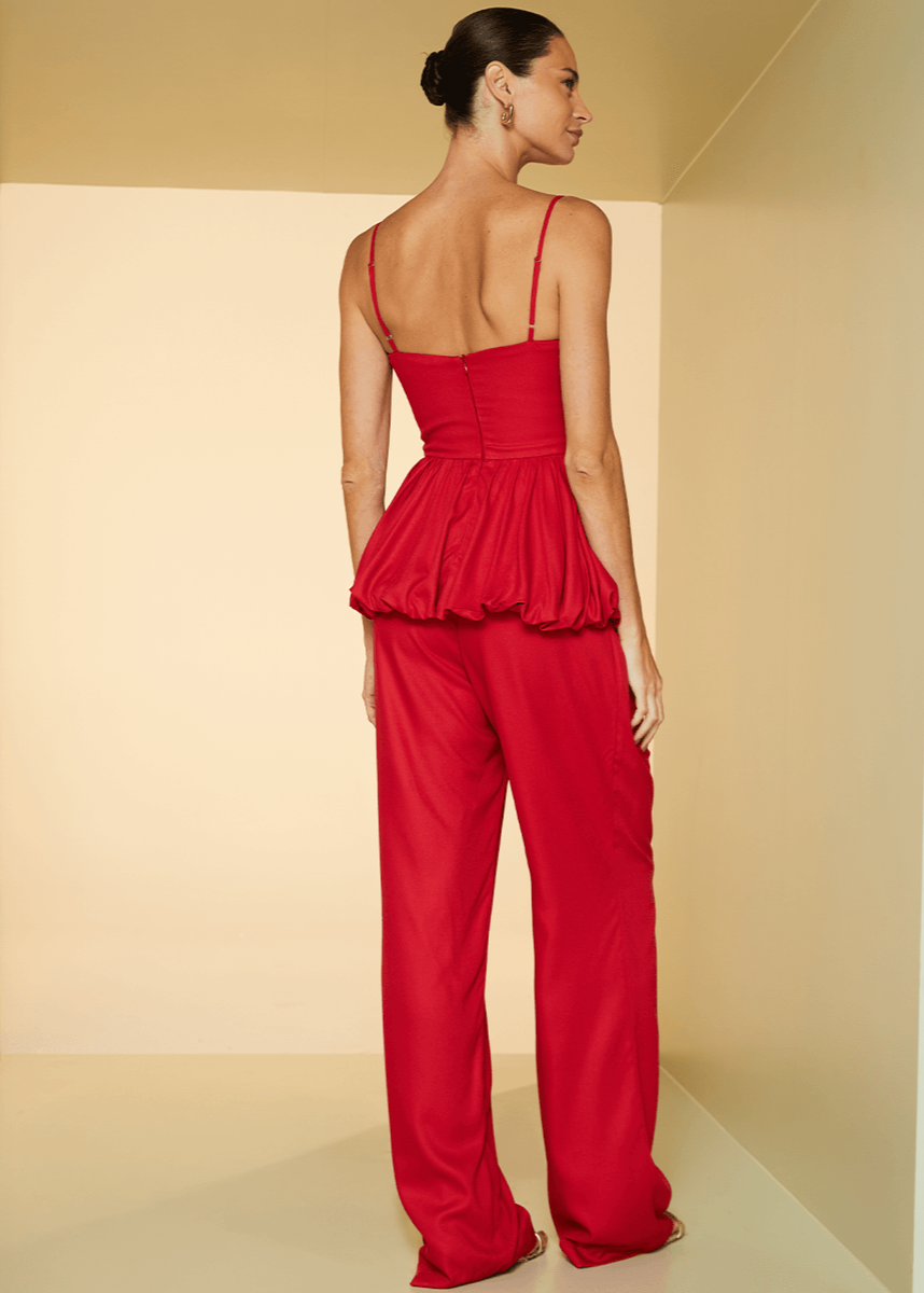 Woman wearing a red jumpsuit standing in a neutral-colored room.