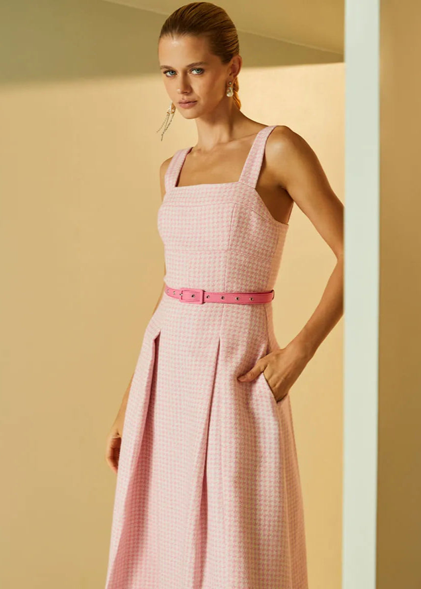 Woman wearing a pink checkered dress with a belt against a beige background