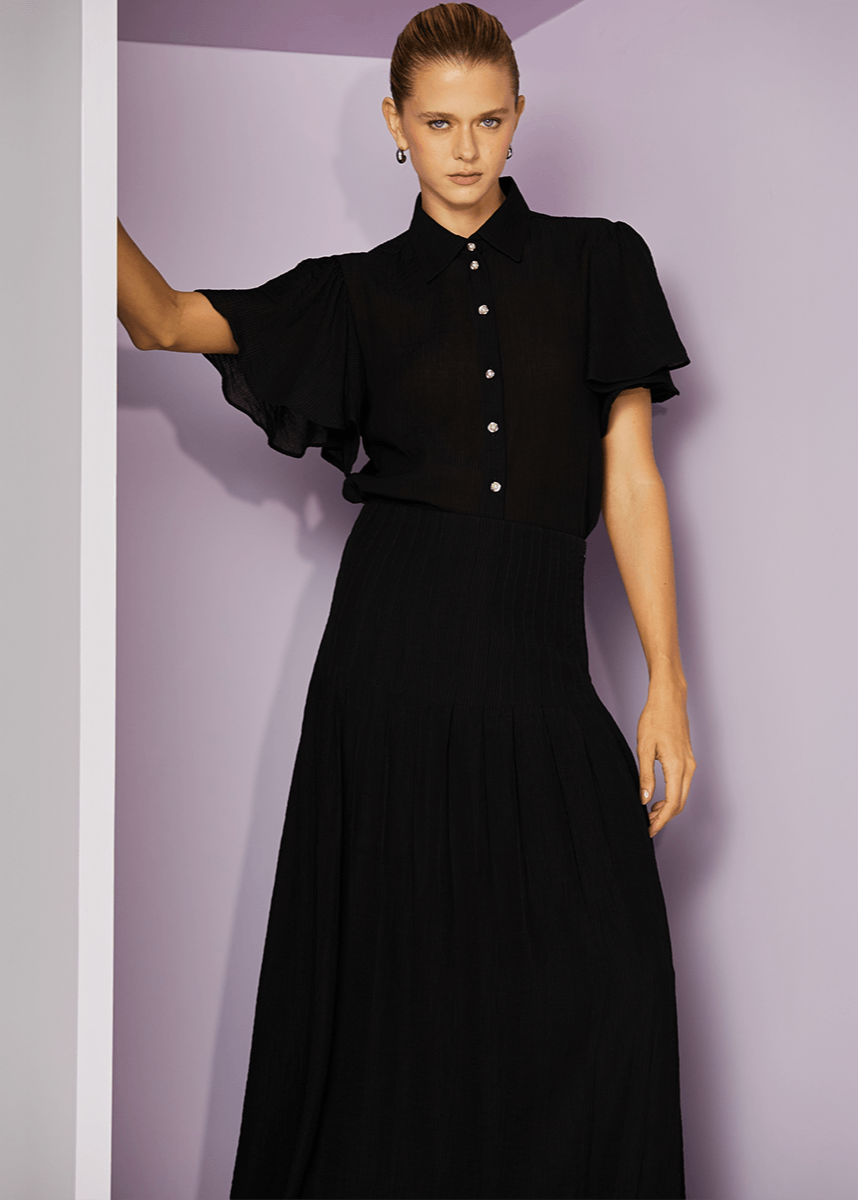 Woman wearing a black dress with ruffled sleeves against a light purple background