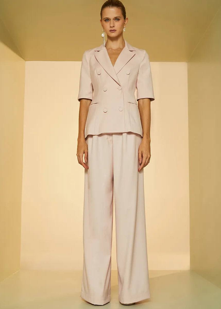 Woman wearing a light pink suit standing against a plain background