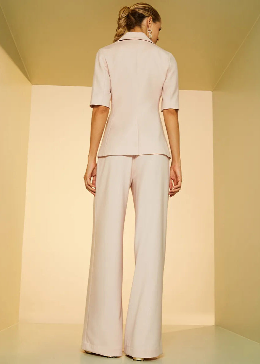 Woman wearing a light-colored outfit standing in a minimalistic room with soft lighting.