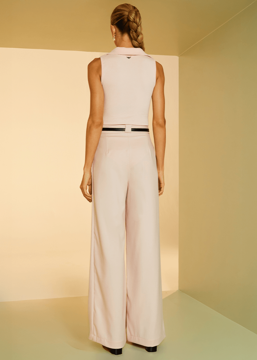 Woman wearing a light pink sleeveless top and wide-leg pants in a minimalistic setting.