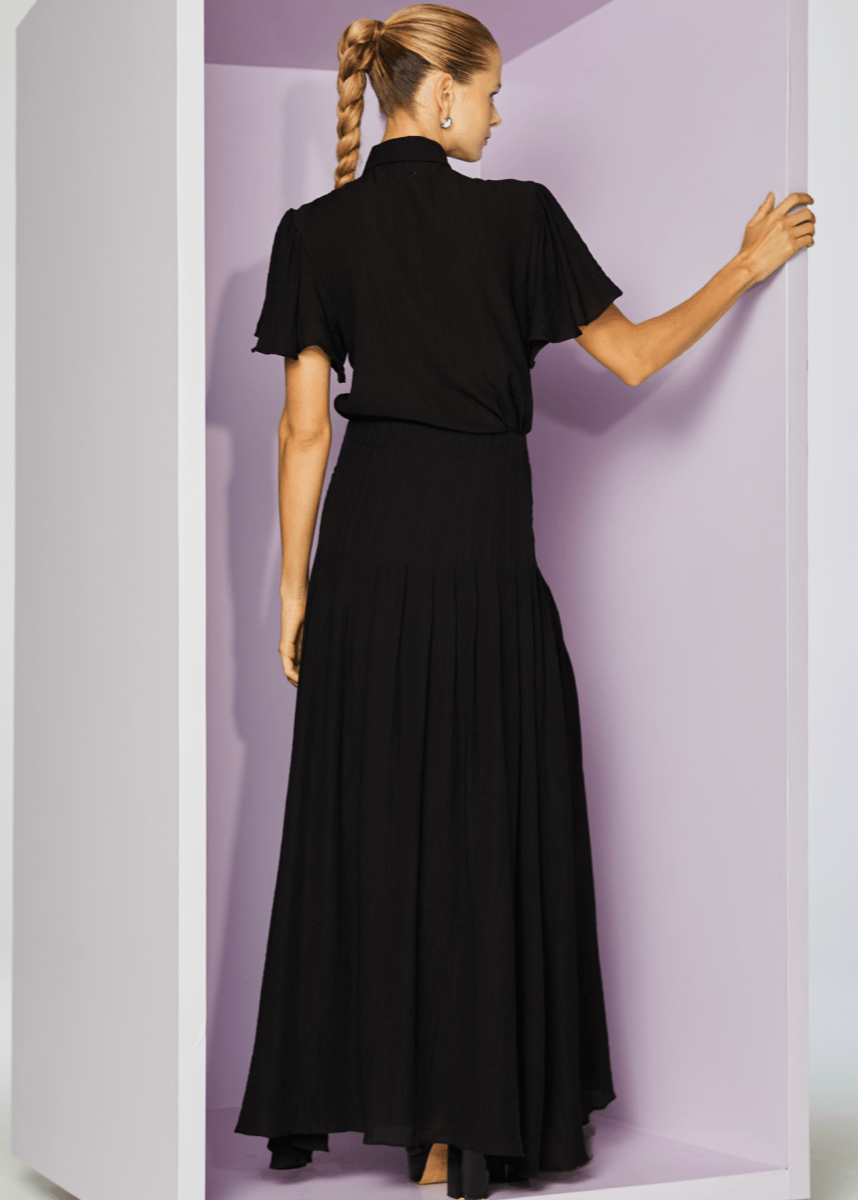 Woman wearing a black dress standing in a minimalistic setting with a white and purple background.