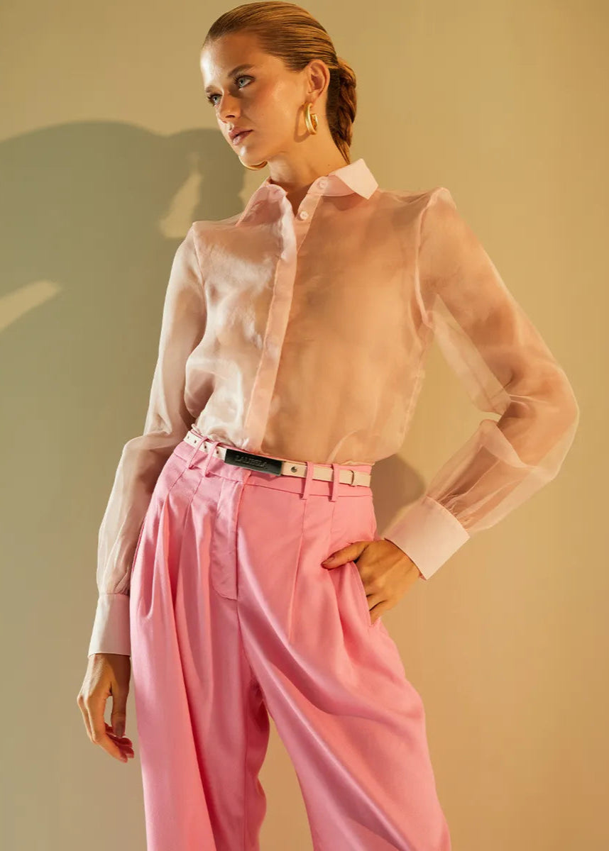 Woman wearing a sheer pink blouse and pink pants against a beige background